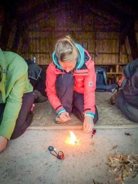 Person entzündet Feuer mit Zündmaterial im Innenraum beim Survival Training