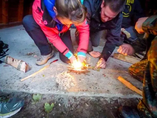Person entzündet Feuer mit Zunder und Holzstücken beim Survival Training