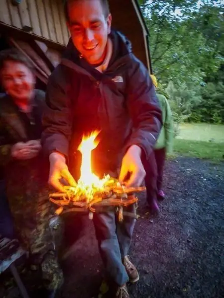 Person hält brennendes Feuerholz in den Händen beim Überlebenstraining