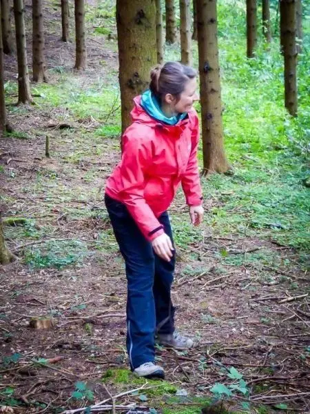 Person in roter Jacke beugt sich im Wald über den Boden