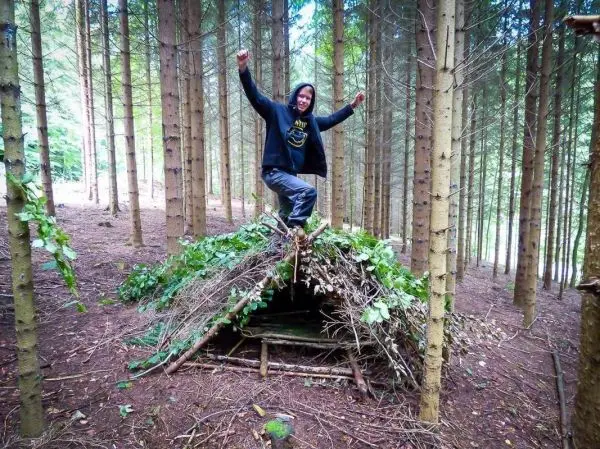 Person steht auf einer selbstgebauten Laubhütte im Wald