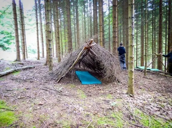 Selbstgebaute Laubhütte aus Ästen mit Unterlage im Wald
