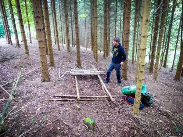 Selbstgebaute Plattform aus Ästen im Wald, Rucksack und Ausrüstung daneben