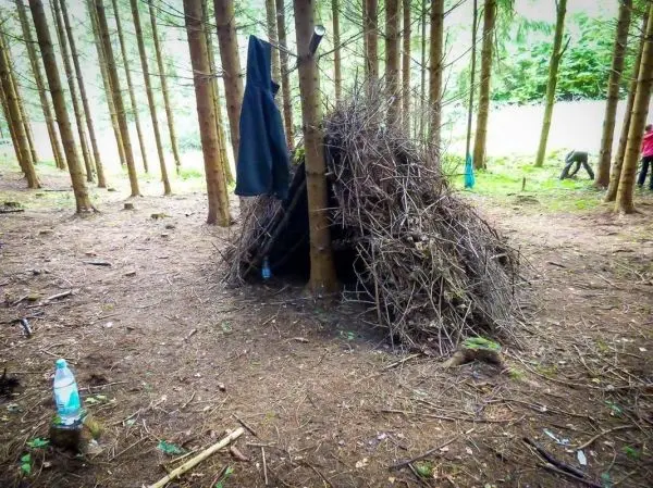 Tarp-Notunterkunft aus Ästen zwischen Bäumen mit Wasserflasche daneben