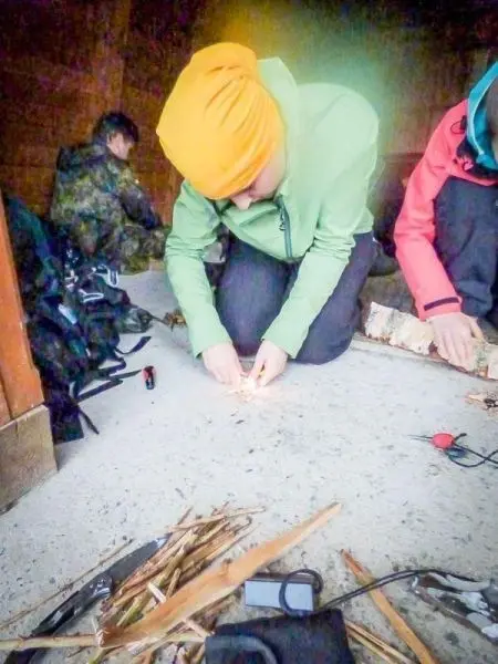 Zunder glimmt auf dem Boden, während eine Person mit einem Feuerstahl arbeitet