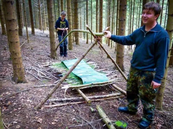 Zwei Personen bauen eine improvisierte Trage aus Ästen und einer Plane im Wald