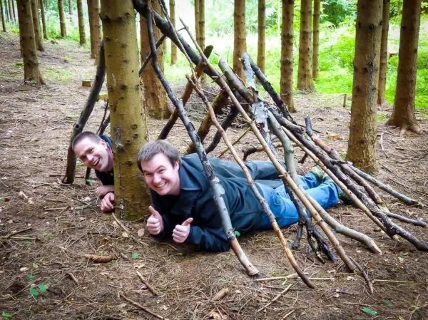 Zwei Personen liegen unter einer selbstgebauten Notunterkunft aus Ästen