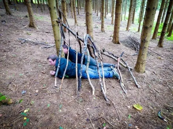 Zwei Personen liegen unter einer selbstgebauten Notunterkunft aus Ästen im Wald