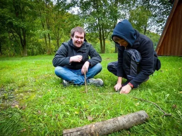 Zwei Personen sitzen auf dem Gras und arbeiten an einer Holzstruktur