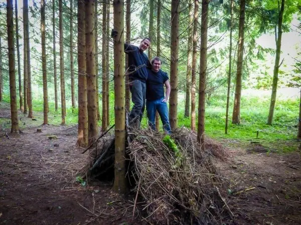 Zwei Personen stehen auf einem Haufen aus Ästen und Zweigen im Wald