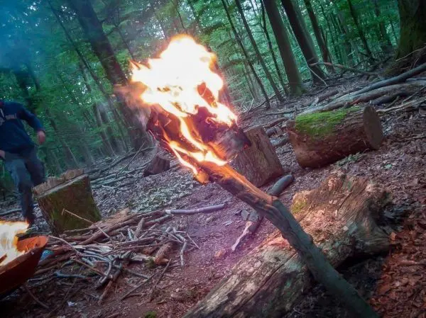 Brennender Stock steht im Wald, Person bewegt sich im Hintergrund