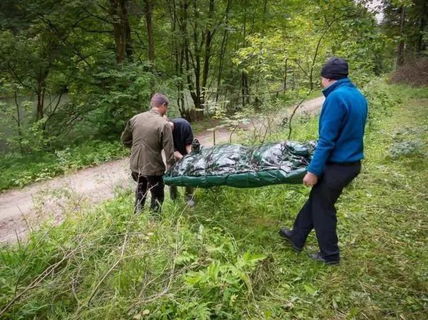 Drei Personen tragen eine improvisierte Trage durch bewaldetes Gelände