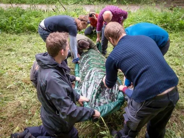 Gruppe hebt eine Person in einer Trage im Wald an