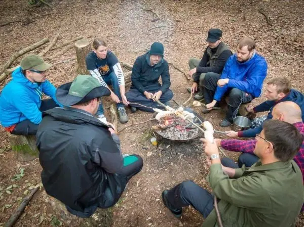 Gruppe sitzt um ein Feuer, während sie Essen auf Stöcken rösten