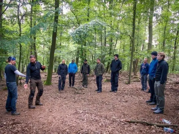 Gruppe steht im Wald, einer erklärt eine Technik mit gestikulierenden Händen
