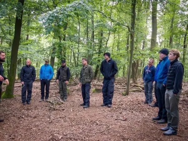 Gruppe steht im Wald und hört einem Vortrag zu