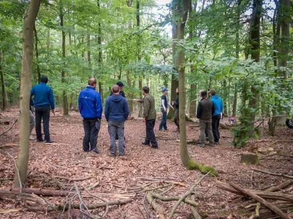 Gruppe steht im Wald zwischen Bäumen und Laub auf dem Boden