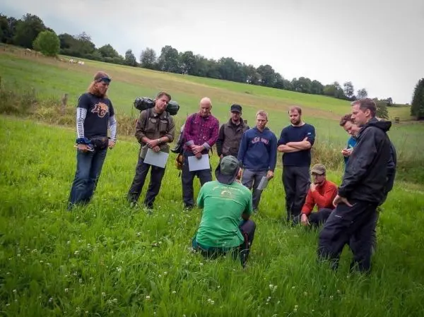 Gruppe von Personen steht im Gras und hört einem Referenten zu