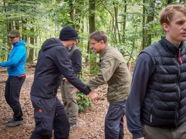 Gruppenteilnehmer üben eine Interaktion im Wald, Hände werden geschüttelt
