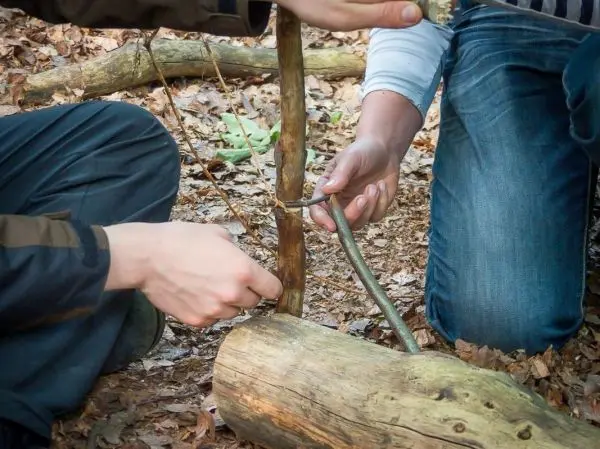Hände binden einen Stock mit Schnur an eine Holzstütze