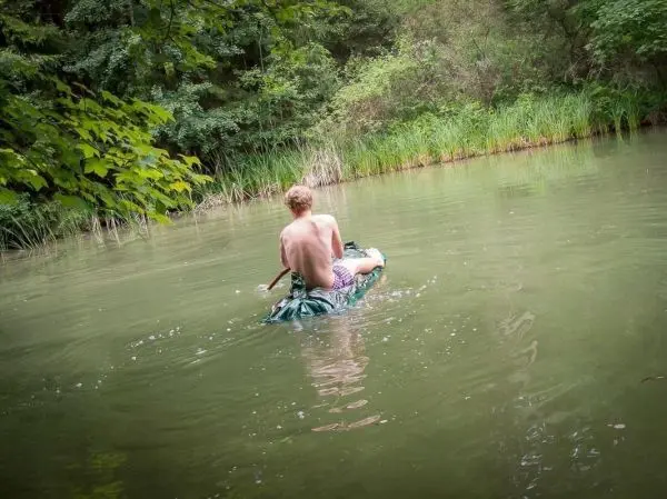 Junge paddelt auf einer improvisierten Schwimmhilfe durch einen ruhigen Gewässerabschnitt