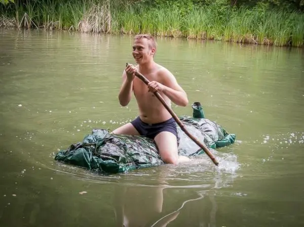 Junge paddelt auf improvisiertem Floß aus Planen im Wasser