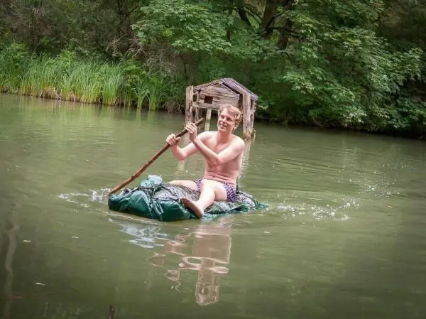 Junge paddelt auf improvisierter Flotte über einen ruhigen Gewässer