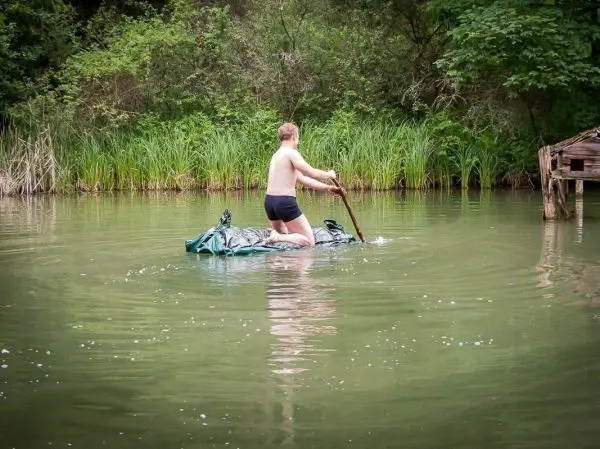 Junge paddelt mit Stock auf improvisiertem Floß im Wasser