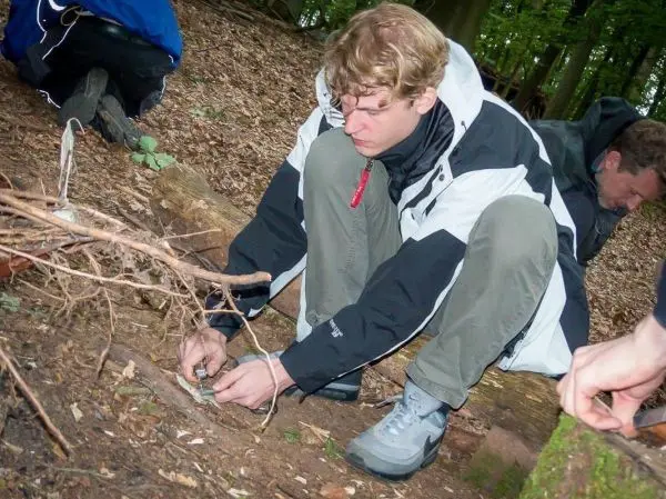 Junger Mann baut eine Schlagfalle im Wald mit Ästen und Schnur