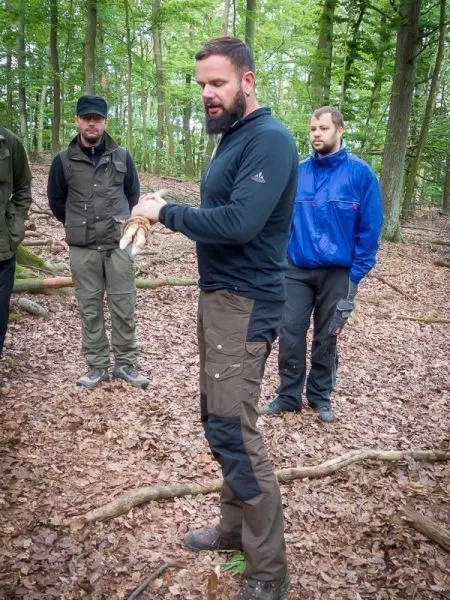 Mann erklärt Techniken im Wald, während andere Teilnehmer aufmerksam zuhören