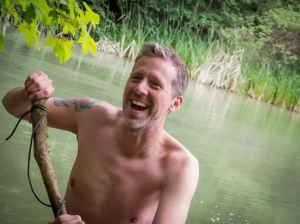 Mann hält einen Stock im Wasser und lacht fröhlich