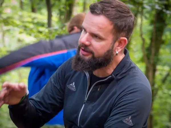 Mann mit Bart gestikuliert im Gespräch in einem Waldgebiet