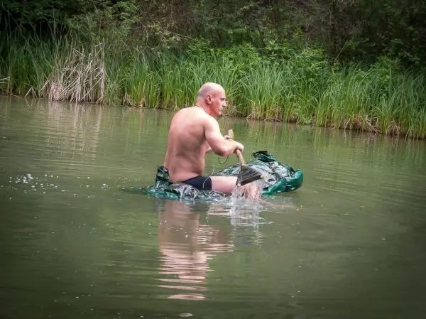 Mann paddelt auf improvisiertem Boot aus Folie im Wasser