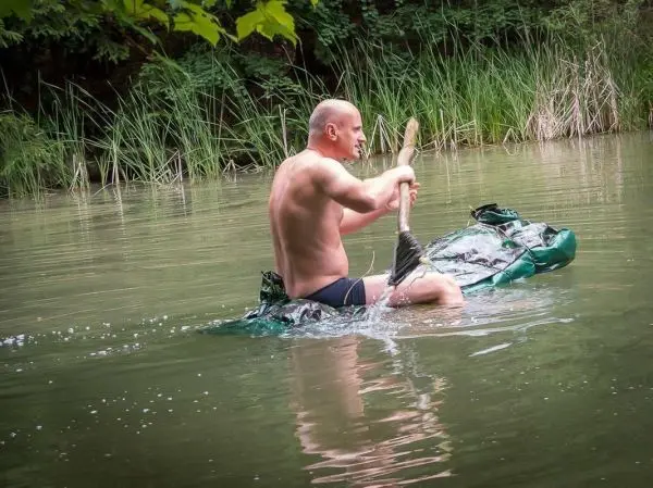 Mann paddelt auf improvisiertem Floß durch einen ruhigen Gewässerabschnitt