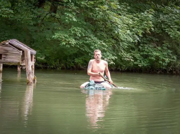 Mann paddelt auf improvisiertem Floß in ruhigem Wasser