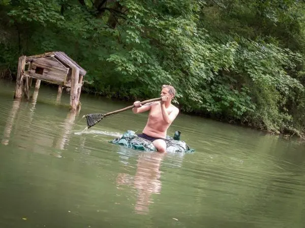Mann paddelt auf improvisiertem Floß mit einem langen Stock im Wasser