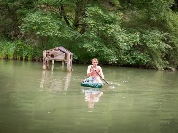 Mann paddelt in einem improvisierten Boot über einen grünen Teich