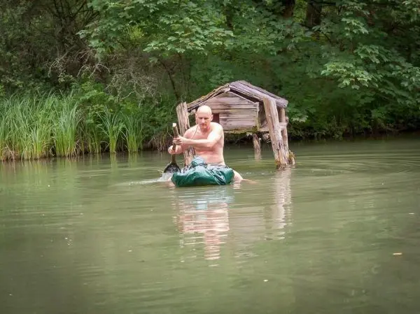 Mann paddelt in einem Wassergefäß durch einen ruhigen Teich