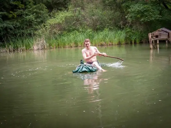 Mann paddelt mit einem Stock auf einer improvisierten Wasserfläche