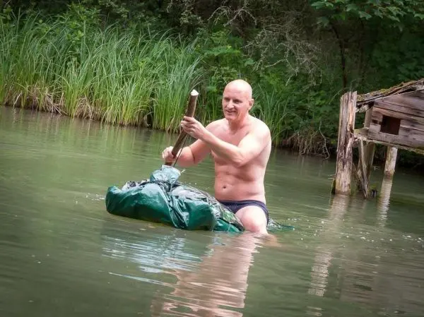 Mann sitzt auf einem grünen Sack im Wasser und hält einen Stock