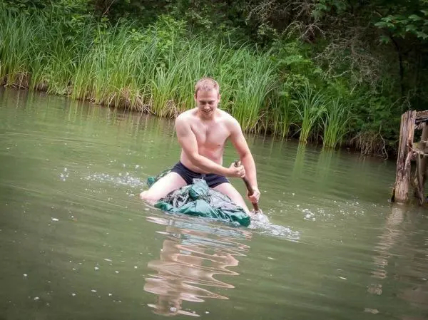 Mann sitzt auf einer improvisierten Schwimmhilfe im Wasser und paddelt mit den Händen
