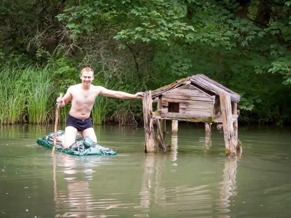 Mann steht auf improvisierter Plattform im Wasser und hält einen Stock