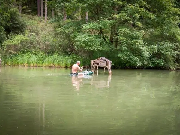Mann steht in einem Gewässer und arbeitet an einem kleinen Holzbau