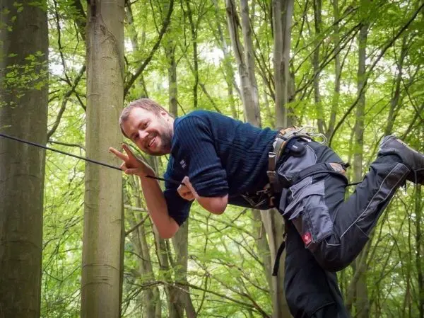Mann überquert eine selbstgebaute Seilbrücke zwischen Bäumen