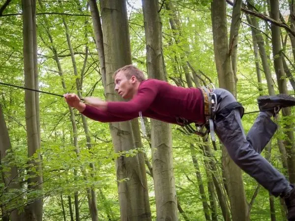 Mann überquert eine selbstgebaute Seilbrücke zwischen Bäumen