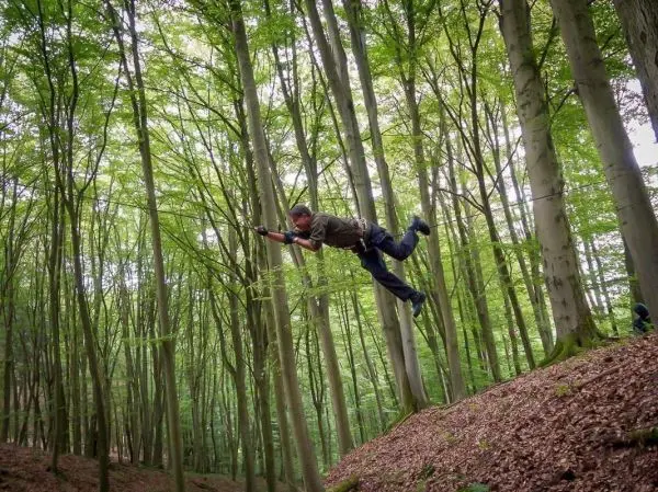 Mann überquert eine selbstgebaute Seilbrücke zwischen Bäumen