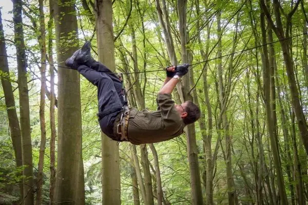 Mann überquert selbstgebaute Seilbrücke zwischen Bäumen im Wald