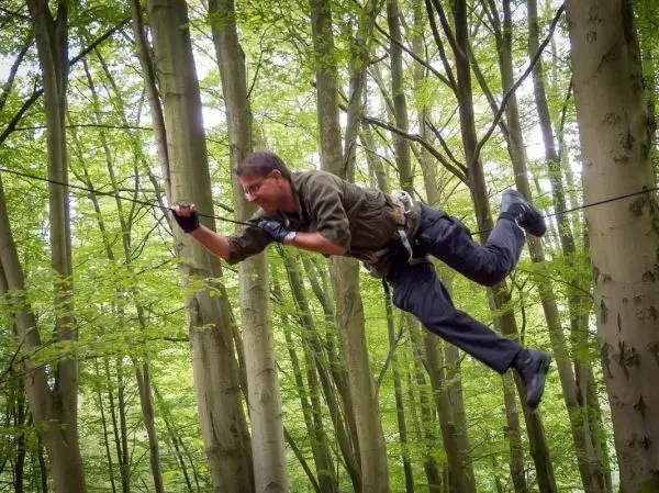 Mann überquert selbstgebaute Seilbrücke zwischen Bäumen im Wald