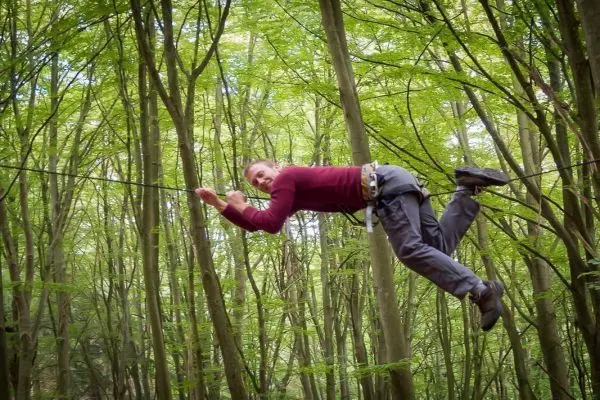 Mann überquert selbstgebaute Seilbrücke zwischen Bäumen im Wald