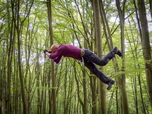 Mann überquert selbstgebaute Seilbrücke zwischen Bäumen im Wald